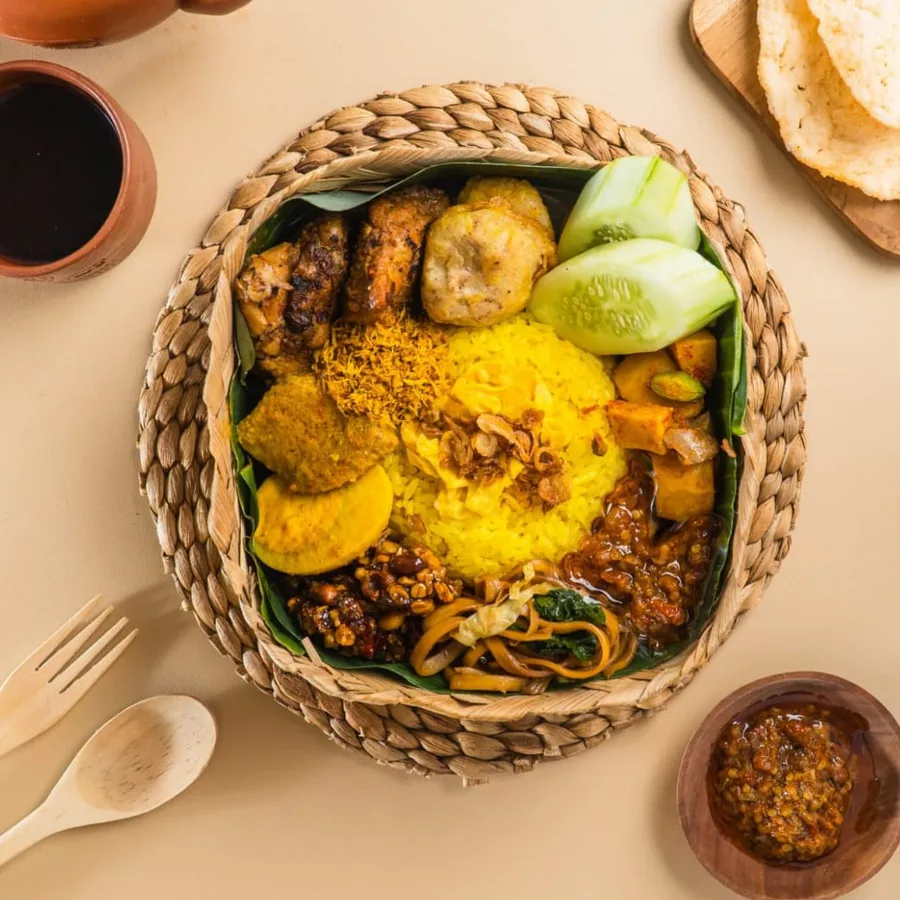 Nasi Kuning lengkap dengan ayam, mie, telur dan kerupuk, disajikan dalam keranjang anyaman