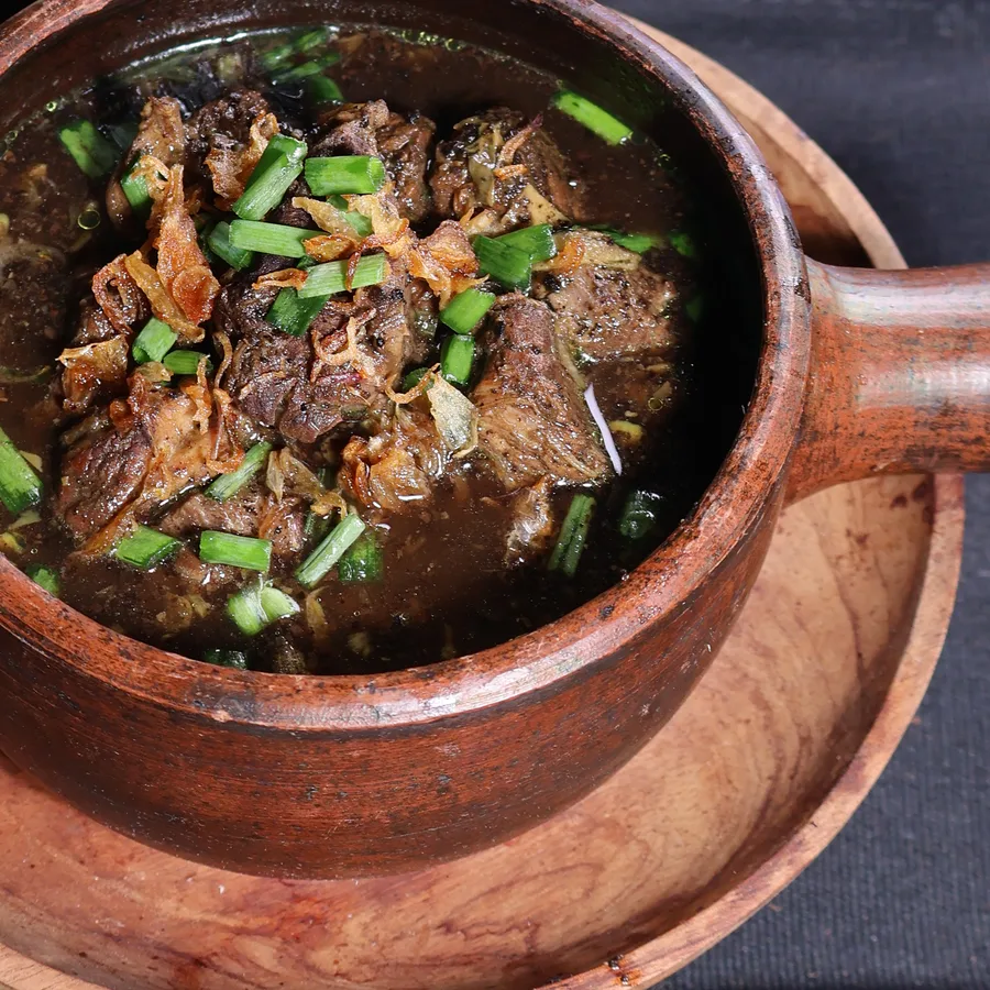 Rawon — kuah kluwek pekat dengan daging sapi empuk, disajikan dalam pot tanah liat bersama telur asin, kecambah dan sambal