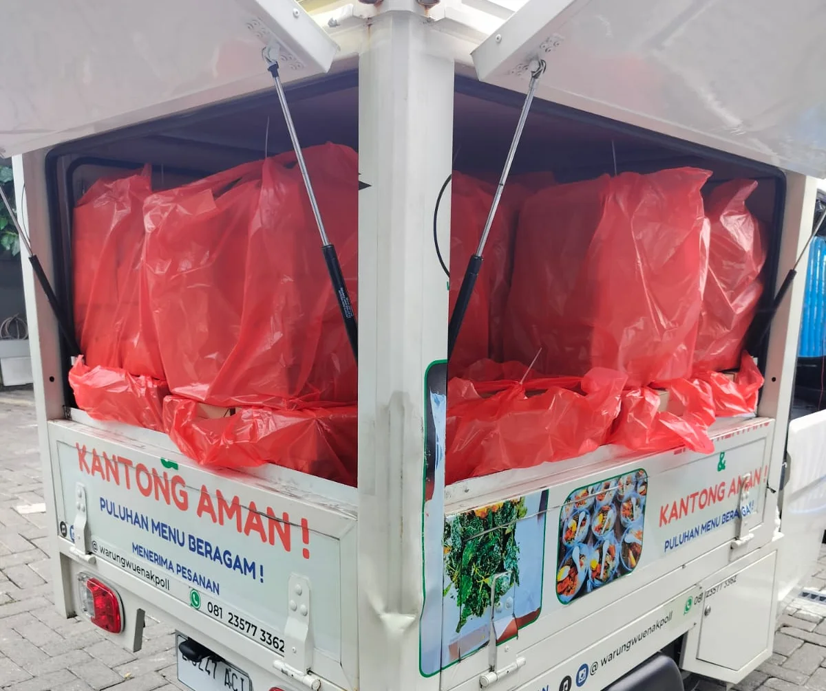 Armada pengiriman Warung Wuenak Poll bertuliskan "Kantong Aman — Puluhan Menu Beragam", bak terbuka dimuati puluhan kantong merah berisi pesanan